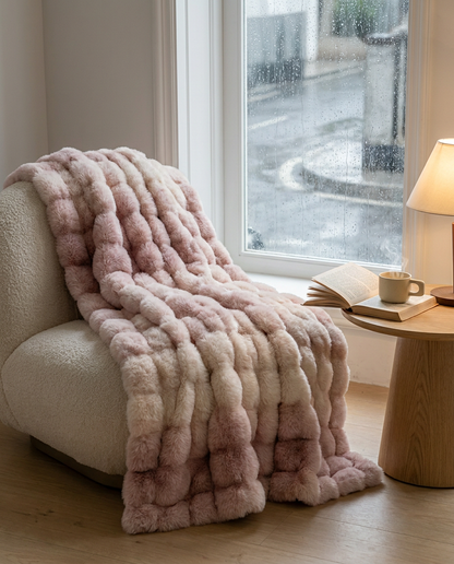 Blush Haze Snuglux blanket draped on an armchair by a rainy window